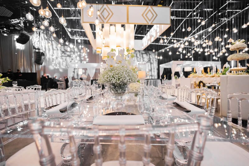 Set table with clear acrylic chairs, crystal glasses and baby's breath under white and gold chandeliers at the Hangar