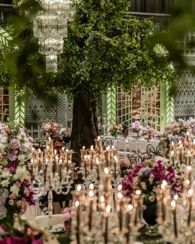 Hangar dining hall with a large tree, crystal chandeliers and candelabras over pink and purple blooms, by mint lattice walls