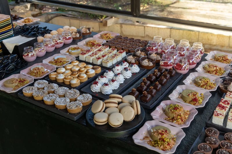 High-angle view of a dessert buffet with rows of mini cakes, tartlets, macarons and mousse cups on black and pink trays