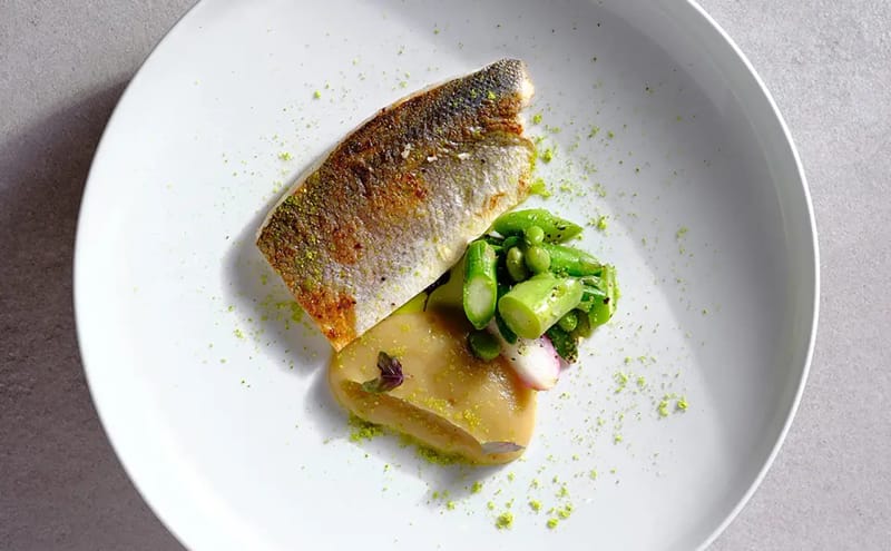 Top-down view of a crisp-skinned seared fish fillet with asparagus, pea salad, pale purée and radish on a white plate