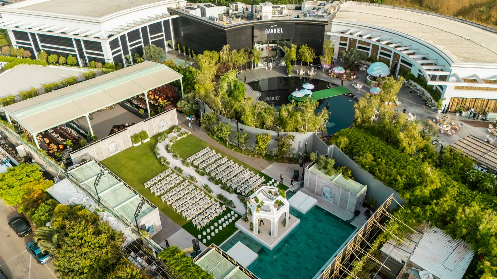 Aerial view of the whole complex: the main building and courtyard pool above, a ceremony lawn with chuppah by a teal pool