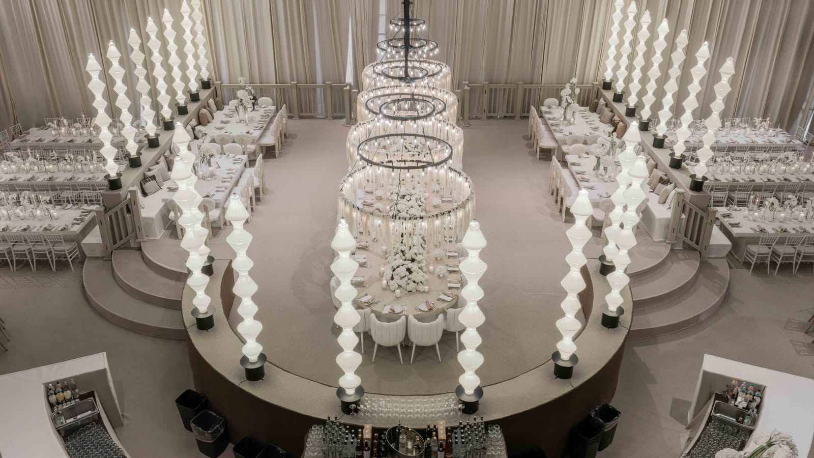 High-angle view of the whole Hangar, with stacked ring chandeliers over an oval table, glowing columns and long tables