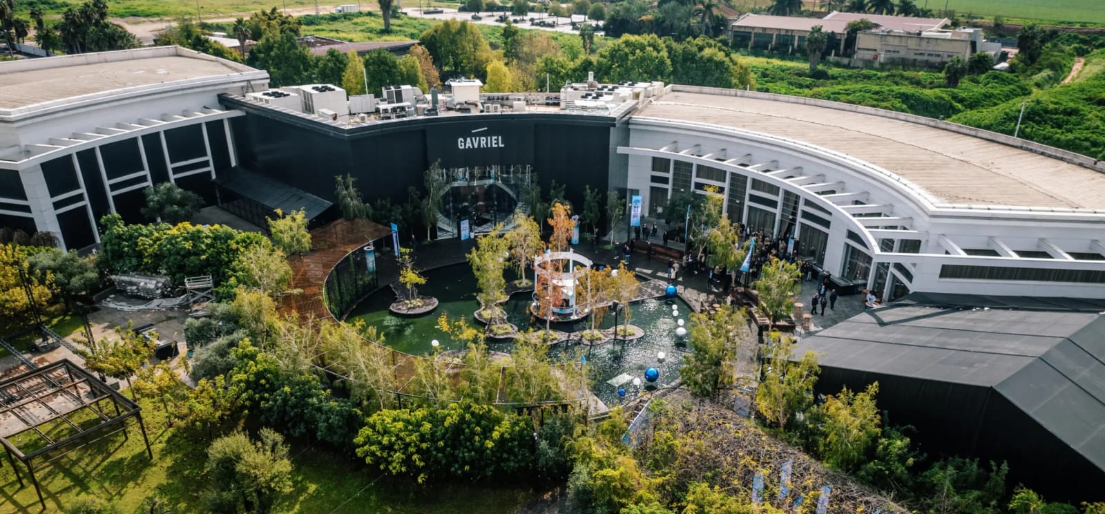 Large panorama de drone d'un bâtiment sombre et courbe avec enseigne sur l'entrée et une cour verte avec bassin et fontaine