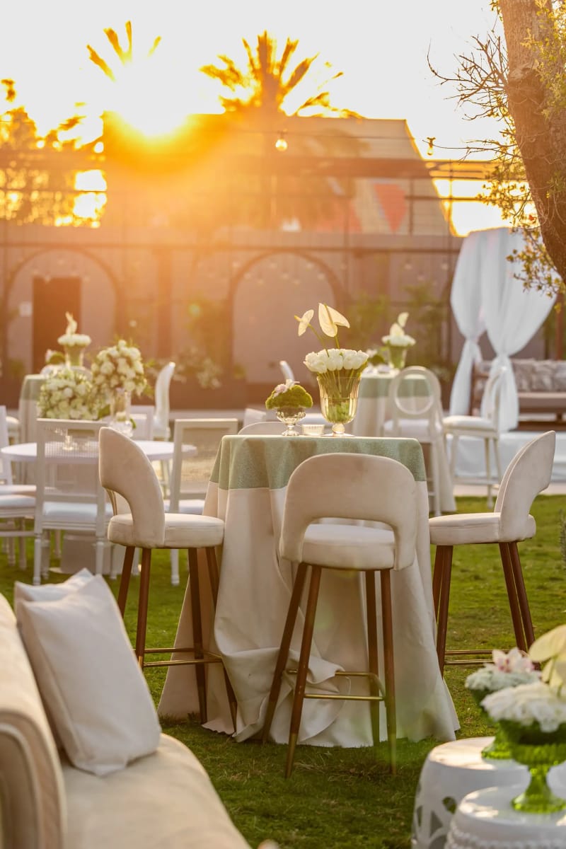 Table de bar jupée de vert sauge, tulipes blanches et chaises de bar crème devant des murs de jardin en arcs, au Bustan