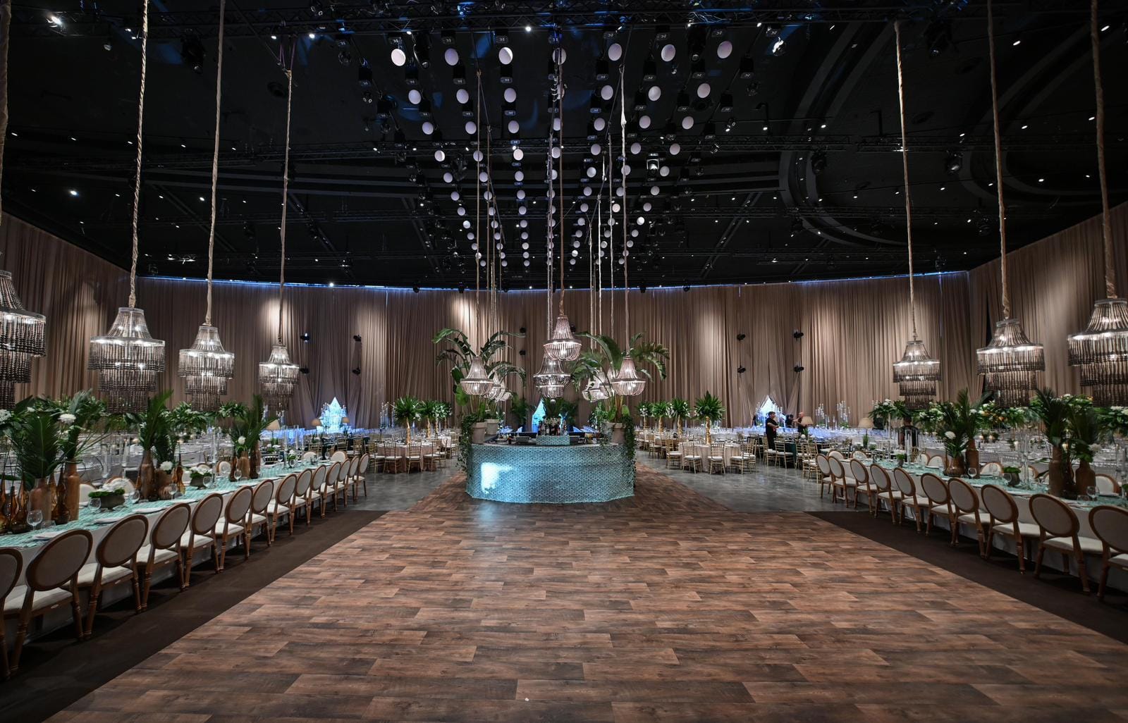 Frontal view of the draped Hangar hall with a dotted ceiling light rig, a parquet aisle, a round bar and long tables