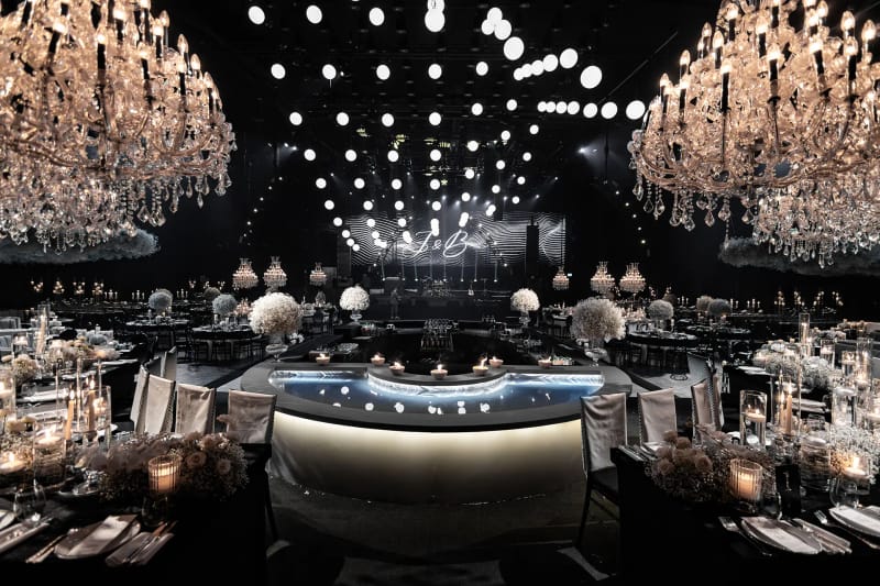 Black Hangar hall with oversized peach-lit crystal chandeliers, a grid of white globes overhead and a circular bar island