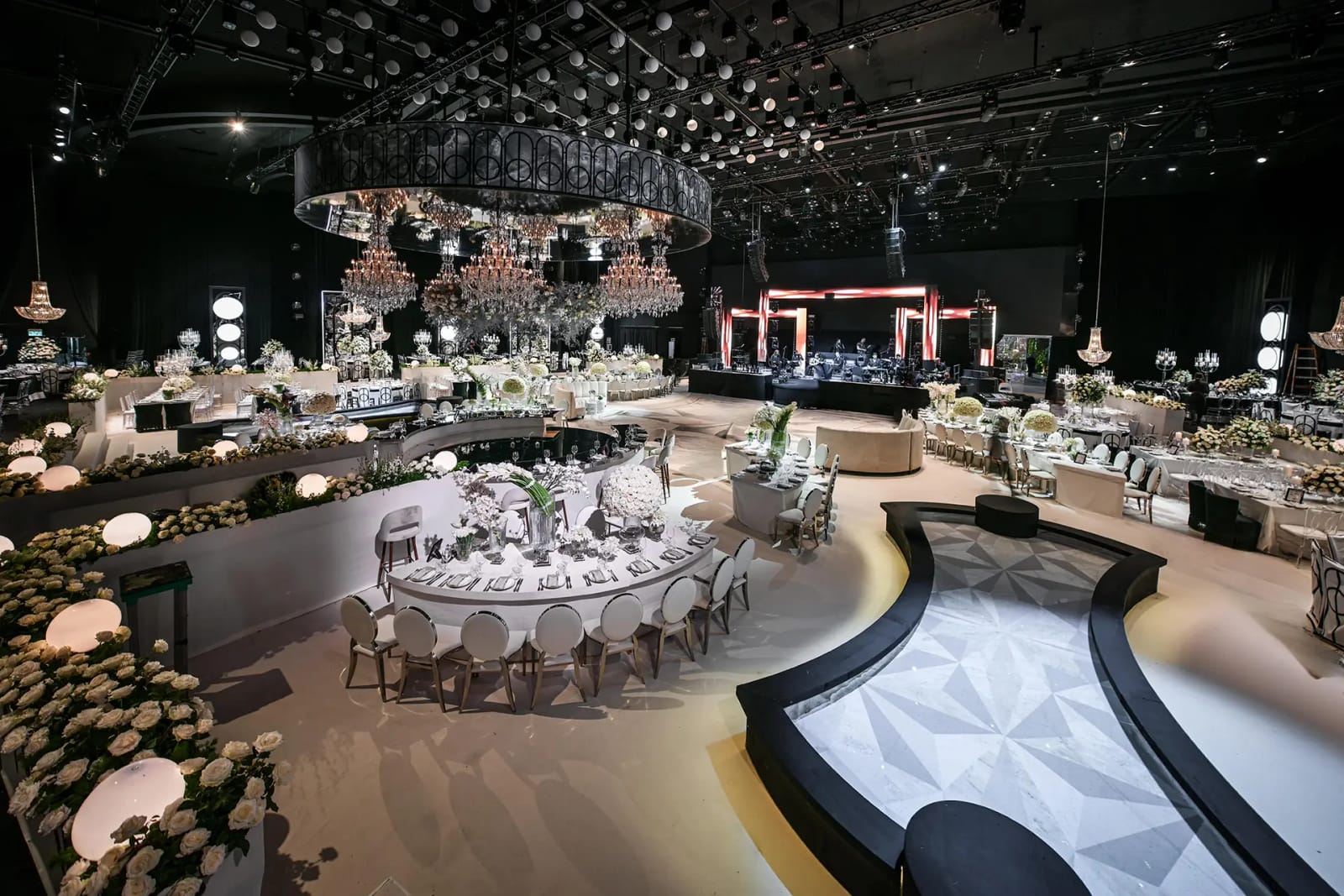 מבט מוגבה על האולם המעוצב בהאנגר, עם שולחנות עגולים, במות לבנות מעוגלות, נברשות טבעת ותקרה גבוהה מאוד