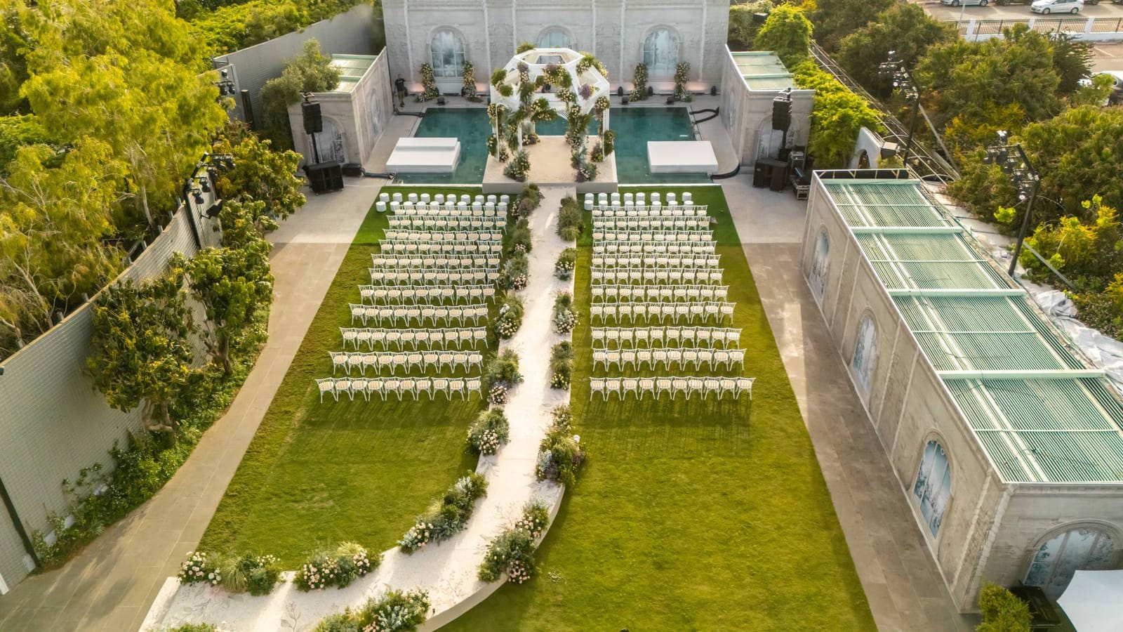 Aerial view of a ceremony at Gavriel: rows of white chairs on the lawn, a flowering path and a pool with a white chuppah