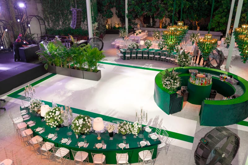 Vue en hauteur le soir d'un événement de jardin sur le thème vert : tables courbes fleuries, bar rond et piste rayée