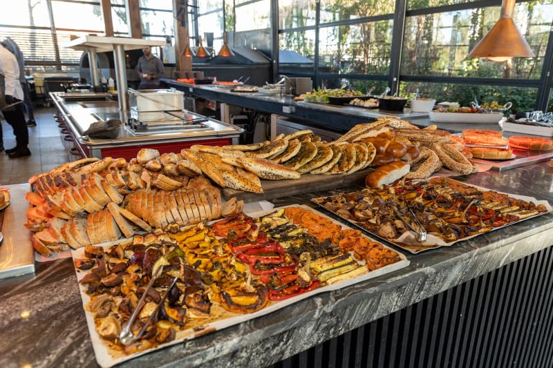 Trays of baked breads, focaccia pastries and roasted vegetables on a marble buffet counter, with copper pendant lamps above