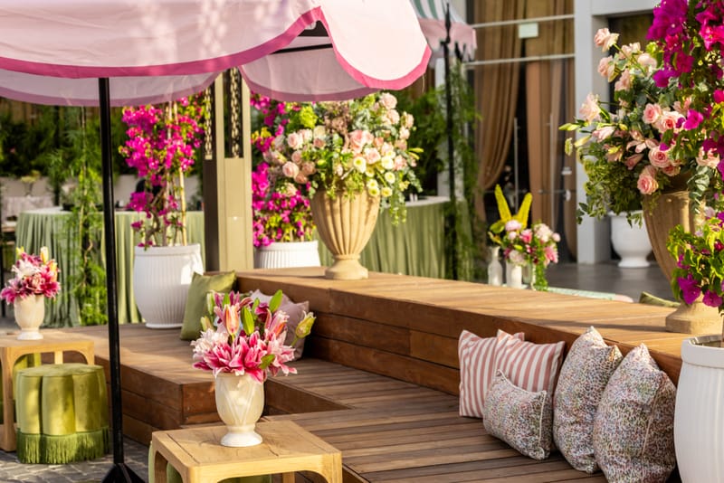 Wooden lounge deck with stone urns, vases of pink lilies and roses, striped cushions and a champagne-coloured curtain