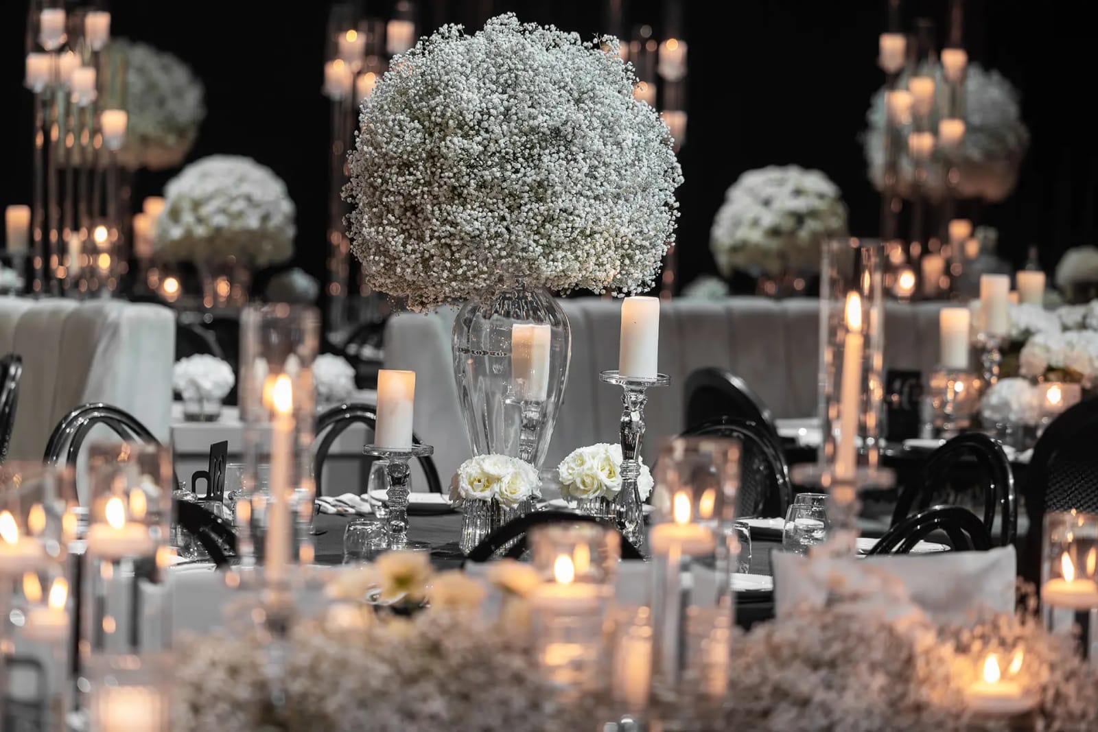 Grande boule de gypsophile et hauts chandeliers sur des tables à nappes noires, avec chaises noires