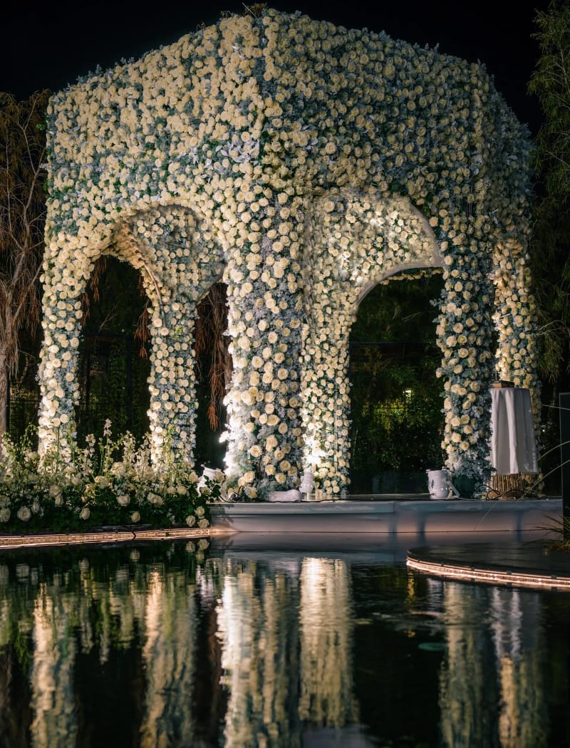 Pavillon à arcades recouvert de fleurs blanches se reflétant dans le bassin la nuit, avec des fleurs blanches au bord