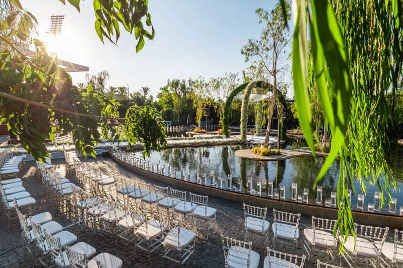 Rangées de chaises blanches le long d'un bassin courbe bordé de bougies, sous des branches de saule, au Bustan