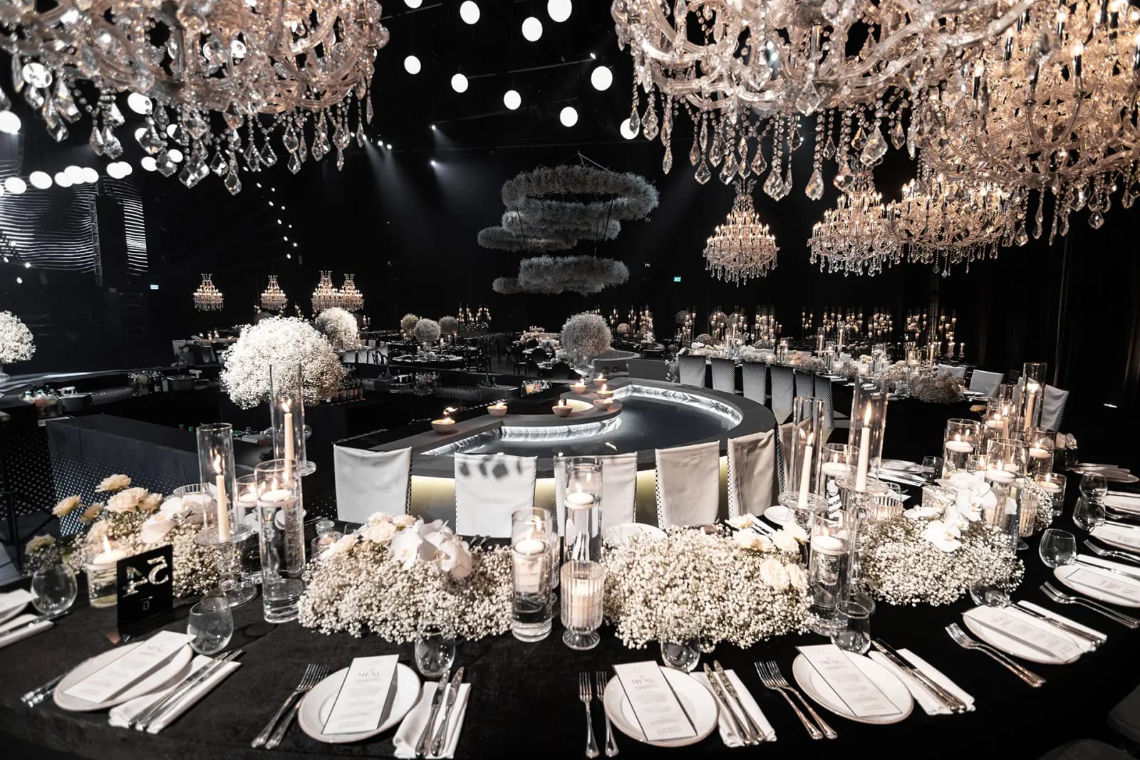 Vue large d'une salle avec lustres en cristal, anneaux de gypsophile et tables dressées autour d'un élément central courbe éclairé