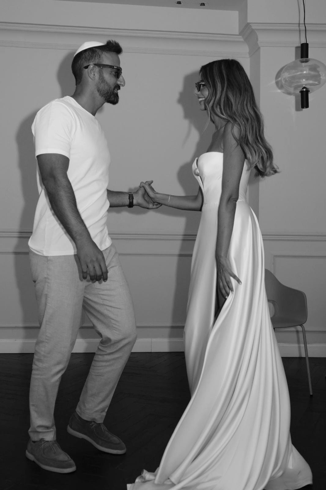 Black-and-white image of a couple dancing hand in hand, he in a white T-shirt, she in a long flowing gown