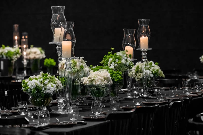 Vases en verre de fleurs blanches et vertes et bougies sous photophores sur une table à nappe sombre