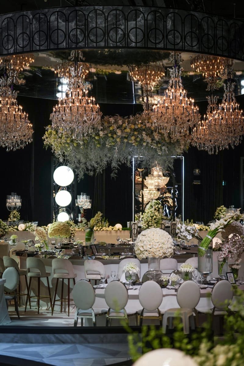 Anneau métallique et lustres en cristal suspendus au-dessus d'un espace de tables rond, globes lumineux, fleurs blanches
