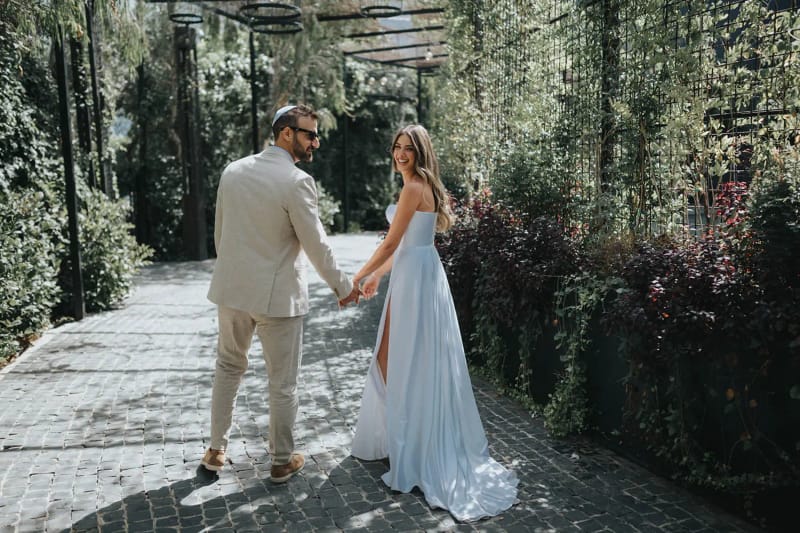 A couple walking hand in hand along a cobbled path between ivy-covered walls under a metal pergola