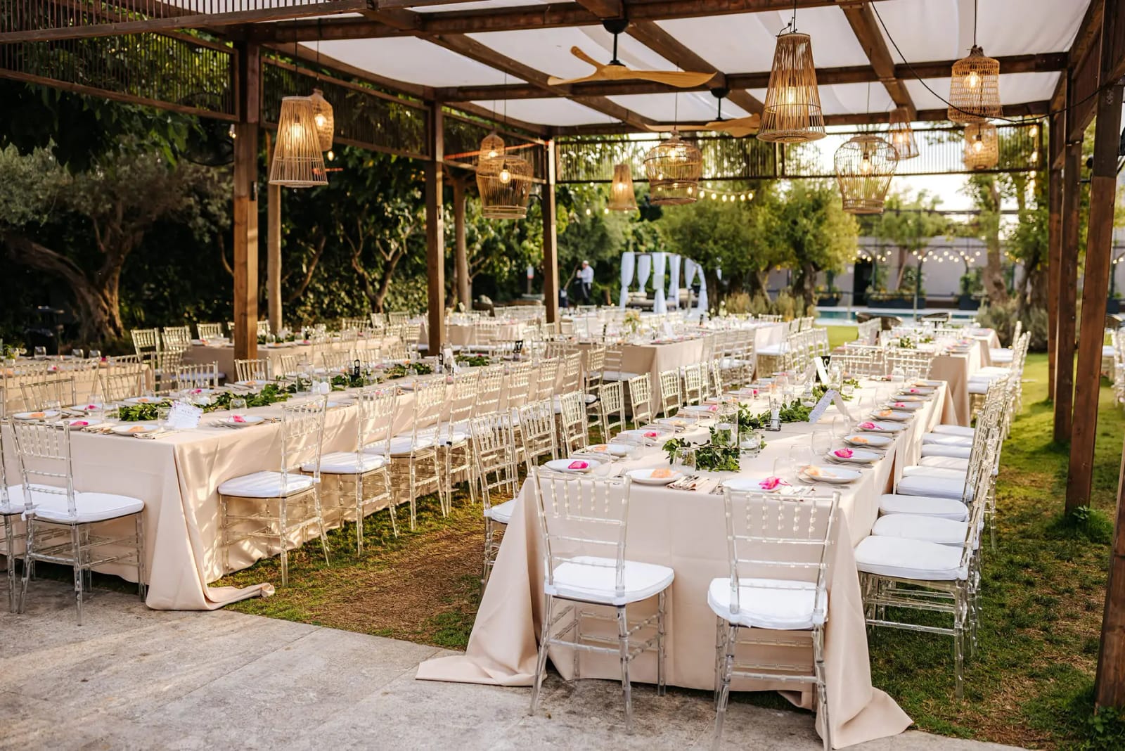Pergola en bois avec suspensions en osier au-dessus de longues tables de banquet dressées en plein air