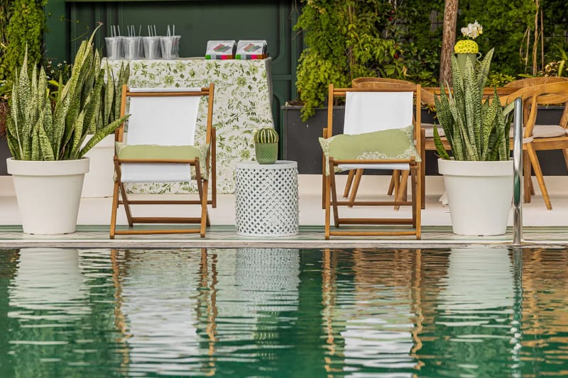 Deux chaises longues pliantes en bois aux coussins blancs et verts entre des sansevierias en pot, au bord du bassin