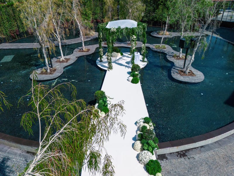 Aerial view of a white path crossing a dark pond to a canopy on an island, among small islands of birch trees
