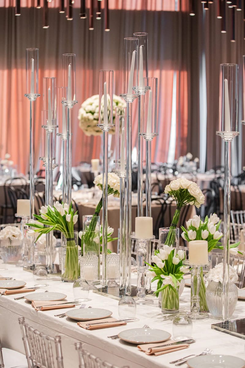 Tall clear glass candle holders, white calla lilies in vases and a blush drape wall behind