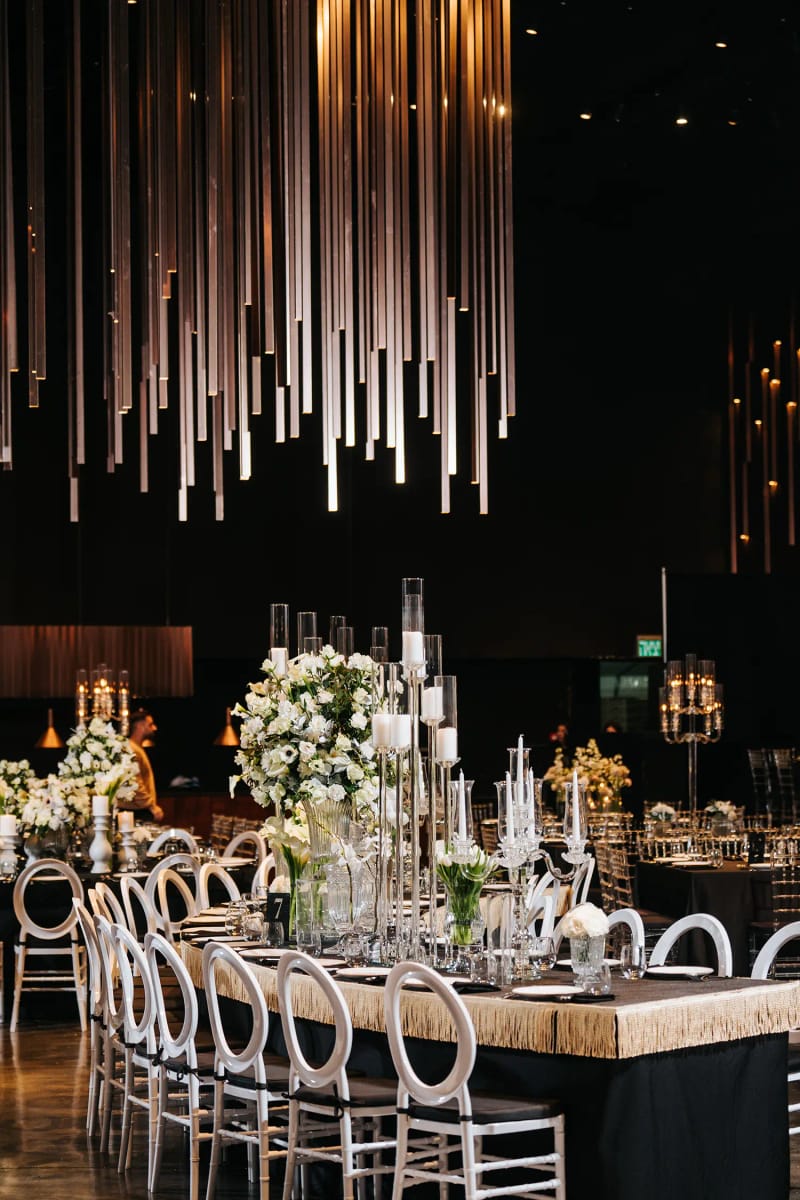 Metallic rods hanging above a long table with white chairs and a white floral arrangement