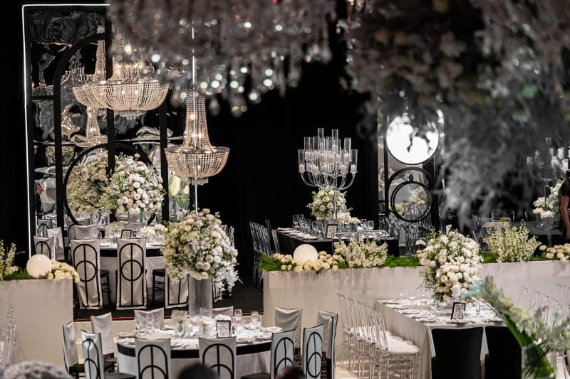 Tables aux compositions de roses blanches, lustres en cristal et chaises à cadre noir, grand panneau rond éclairé au fond
