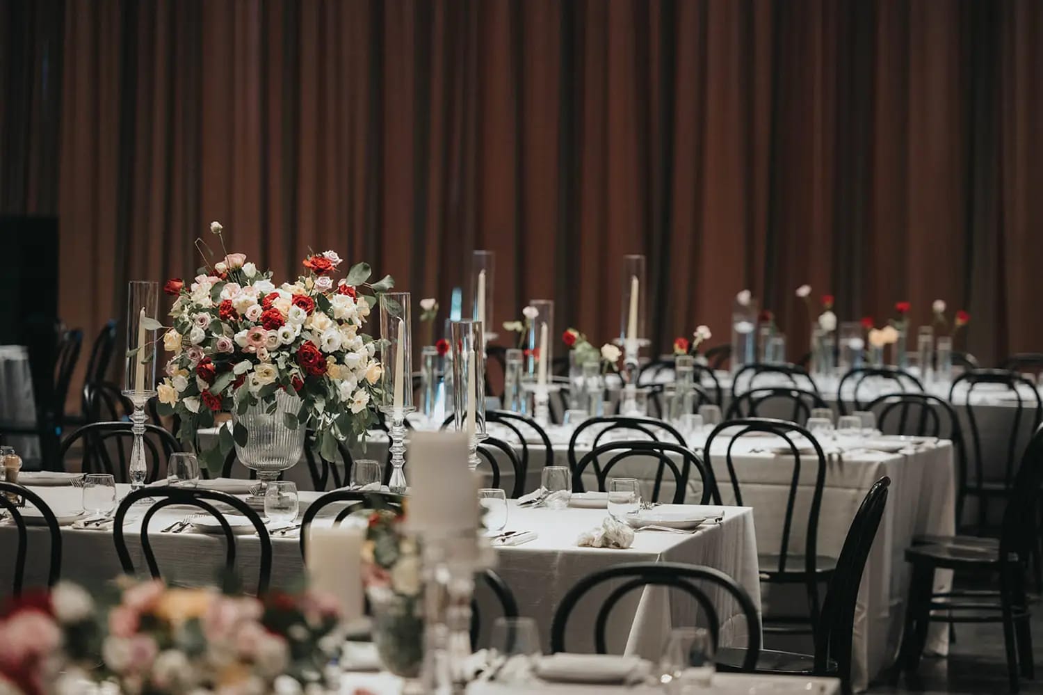 Tables au Shulhan nappées de blanc, chaises bistrot noires et fleurs rouges et blanches, décor Cozy Glamour