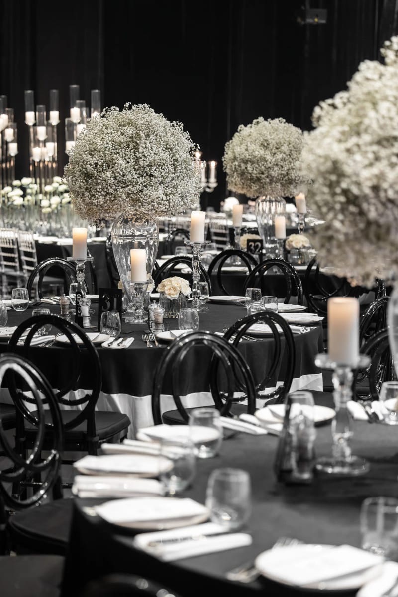 Tables dressées avec nappes noires, assiettes blanches, bougies et grosses boules de gypsophile