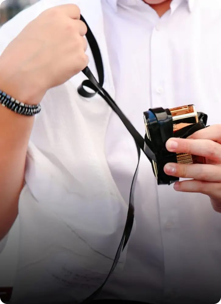 Une personne en chemise blanche tenant des tefillin, un petit boîtier noir aux lanières de cuir noir pendantes