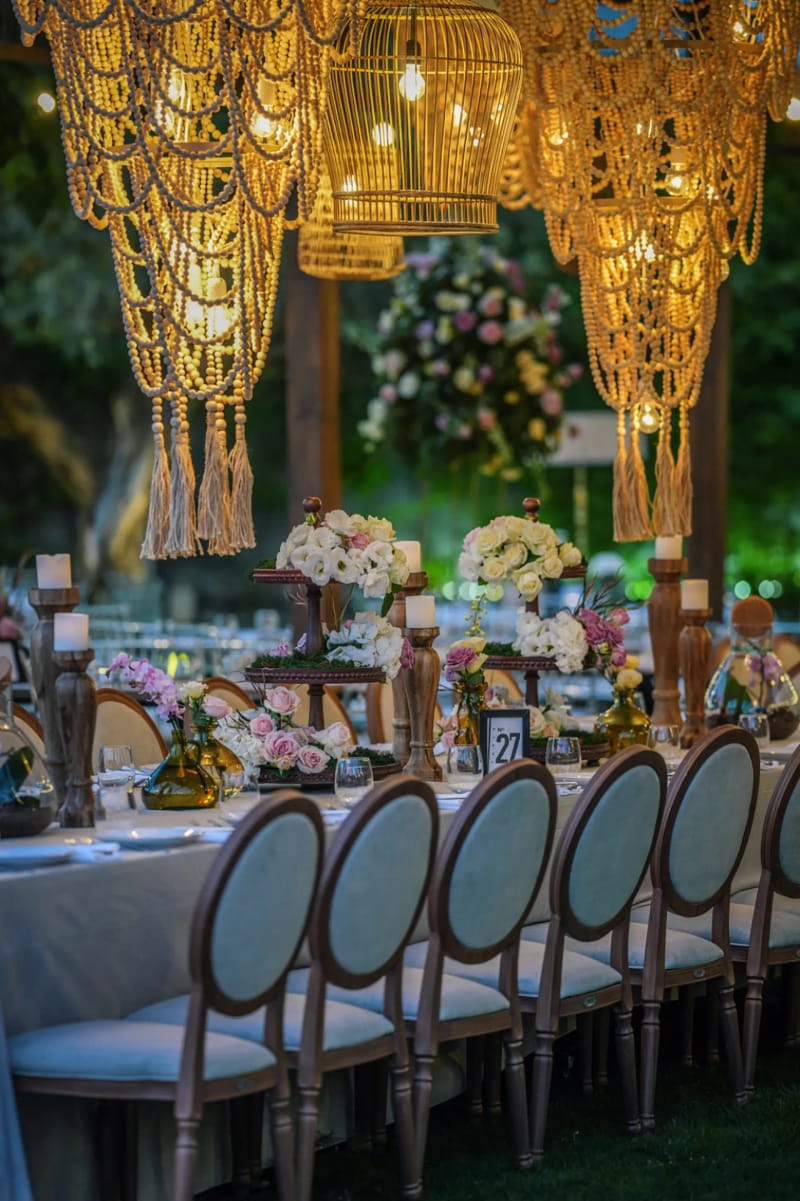 Woven beaded pendant chandeliers above a long table with round-back chairs and flower arrangements
