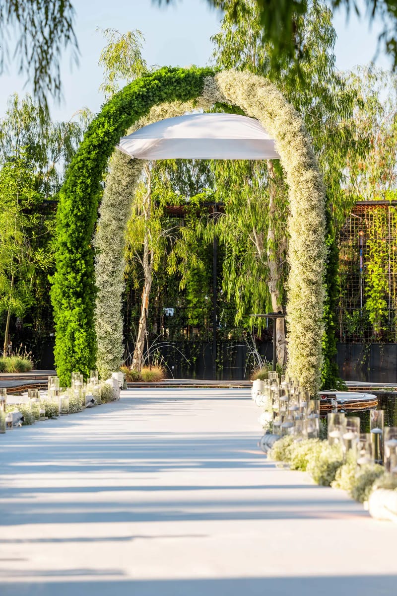Arche de verdure et de fleurs blanches au-dessus d'une allée blanche bordée de fleurs, parmi les saules, Majestic Serenity