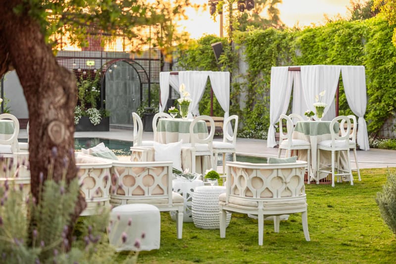 Canapés et chaises blancs et deux cabanes drapées sur la pelouse près d'un mur de lierre