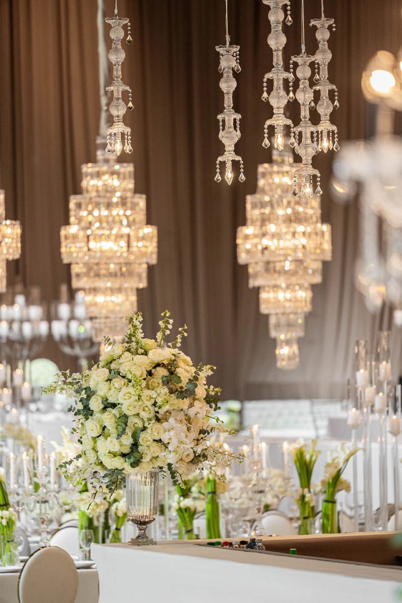Lustres en cristal suspendus au-dessus d’un grand bouquet blanc, avec bougies et tables dressées derrière