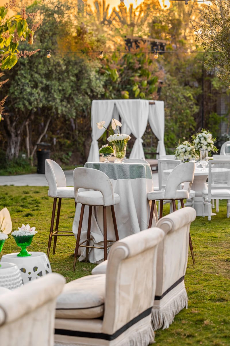 Coin salon sur la pelouse avec canapés blancs, tables de cocktail et cabane drapée dans la lumière du couchant