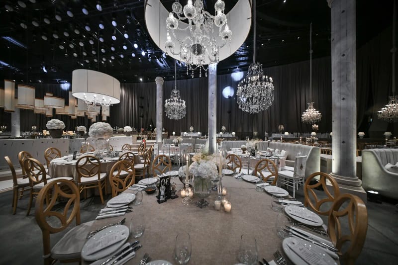 Table ronde dressée avec chaises en bois, grand lustre globe blanc et suspensions cylindriques entre des colonnes en béton