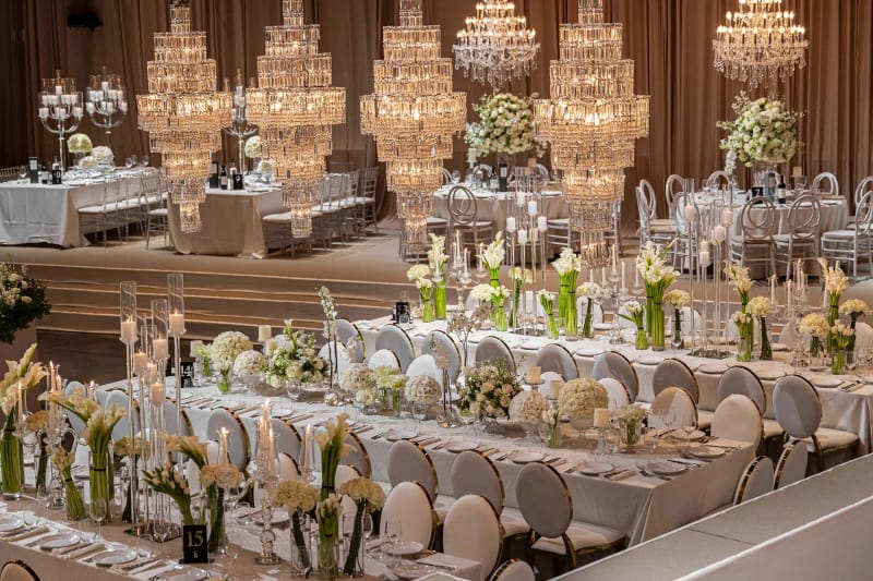Longues tables ornées de callas blancs et de bougies sous une rangée de lustres en cristal étagés