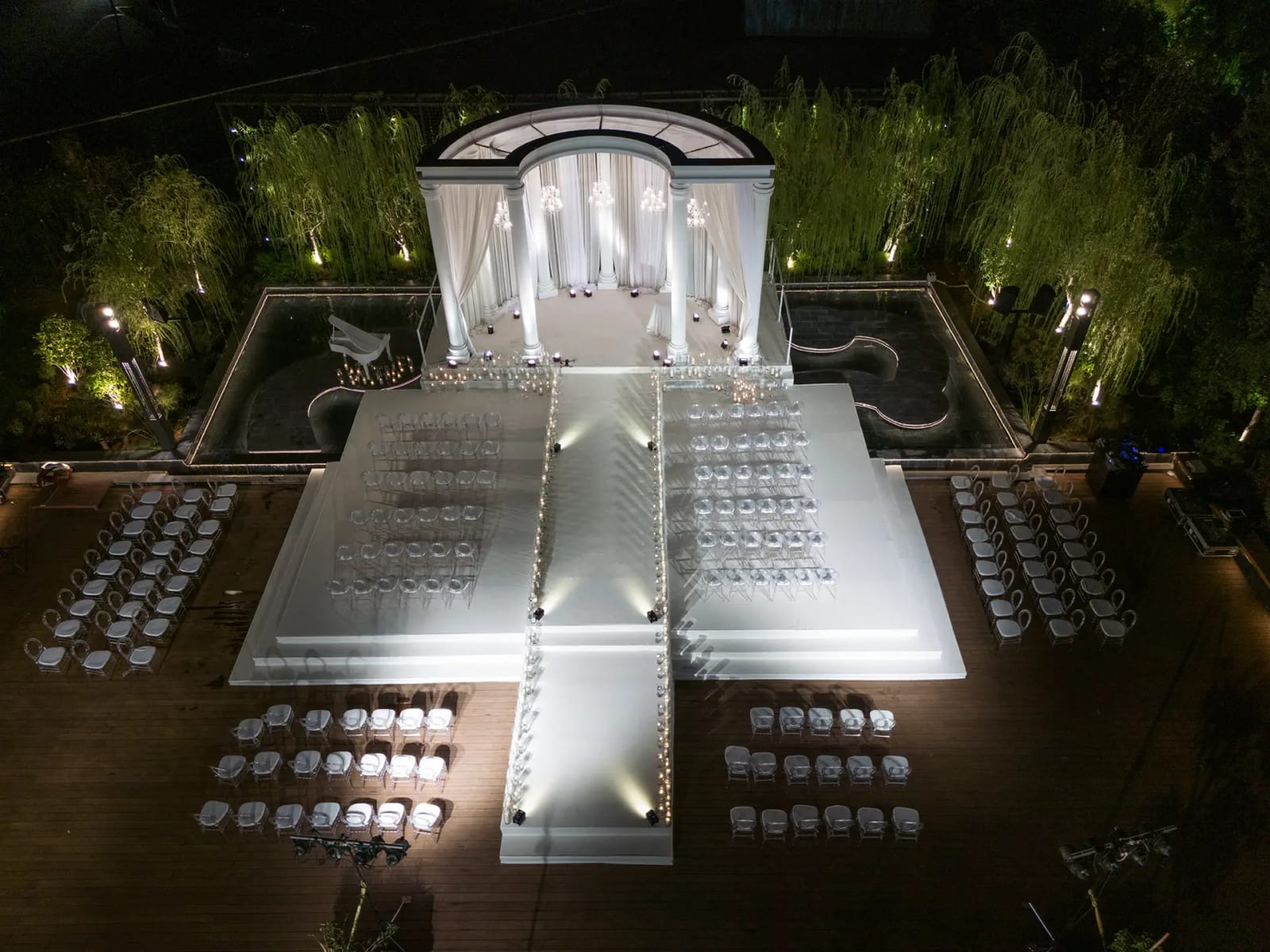 Vue aérienne de nuit d'une estrade blanche en croix, chaises de chaque côté et pavillon à colonnes au fond
