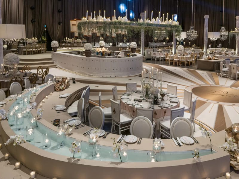Tables de banquet courbes étagées avec un chenal éclairé bleu pâle, couronne de bougies suspendue et sol à rayons