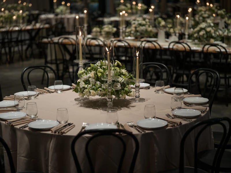 Round table set with a taupe cloth, plates and glasses, and a green-and-white centerpiece with taper candles