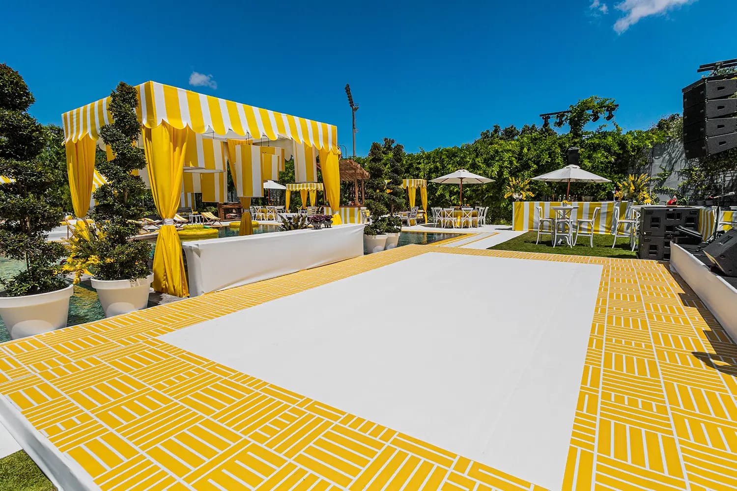 Rectangular floor with a yellow pattern border and white center in front of a yellow-draped canopy, under a blue sky