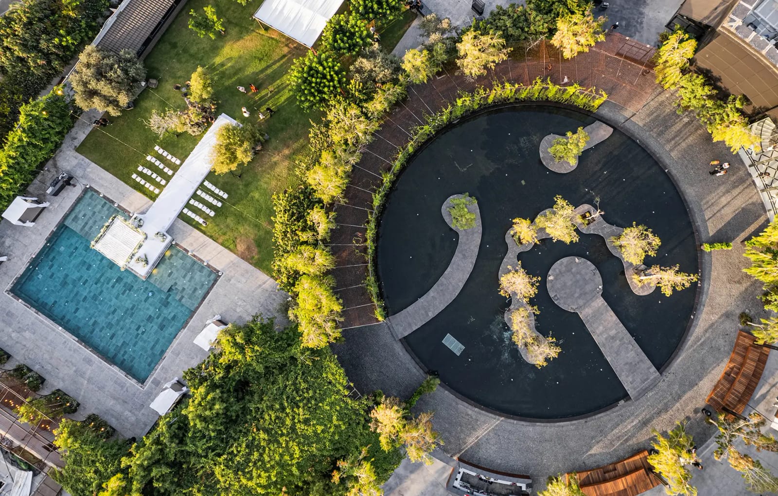 Vue aérienne d'un bassin noir circulaire au chemin de pierre sinueux, d'une piscine turquoise et d'une pelouse