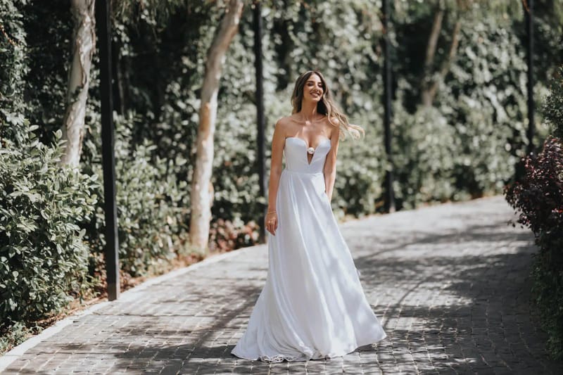 A bride in a white gown standing on a cobbled path between ivy walls and trees