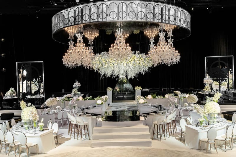 Anneau de lustres avec installation de fleurs blanches au-dessus d'une estrade ronde surélevée, entourée de tables blanches