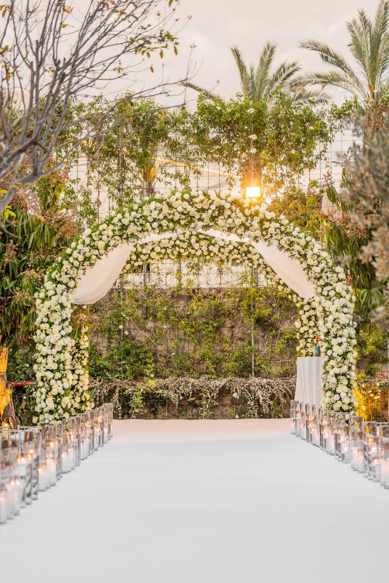 Grande arche couverte de fleurs blanches et de feuillage dans le jardin, avec allée blanche et lanternes