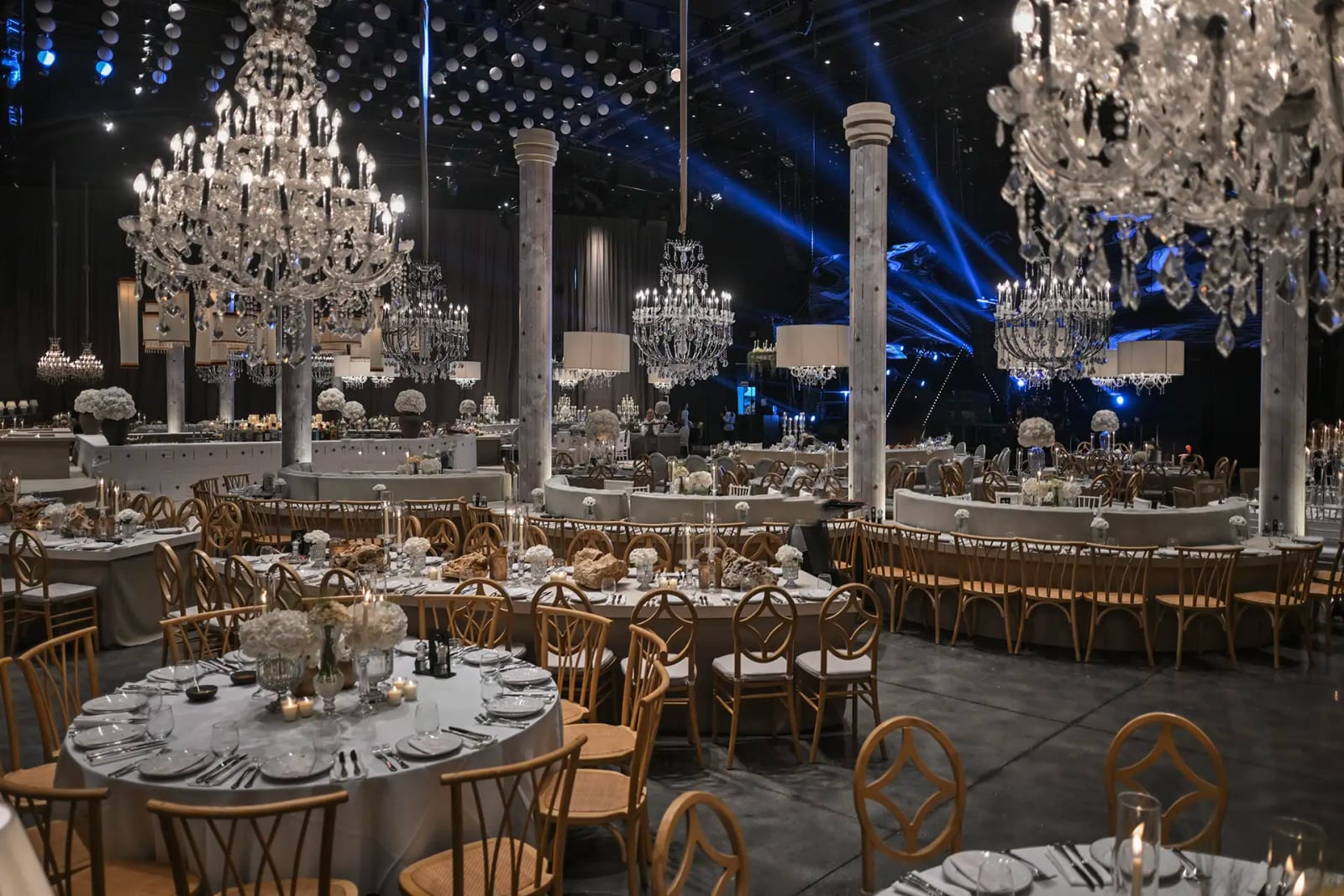 Salle avec grands lustres en cristal, tables rondes et faisceaux de lumière bleue entre des colonnes