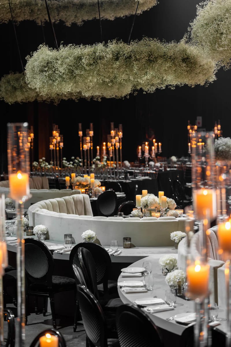 Anneau suspendu de gypsophile au-dessus de tables rondes à nappes noires, banquette courbe blanche et hauts photophores
