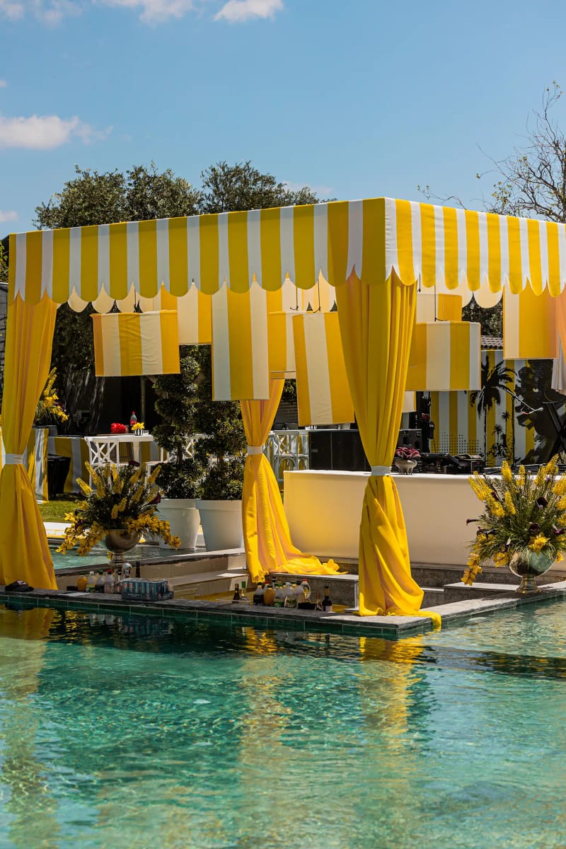 Yellow and white striped canopy with yellow curtains on a platform in the pool, under a blue sky